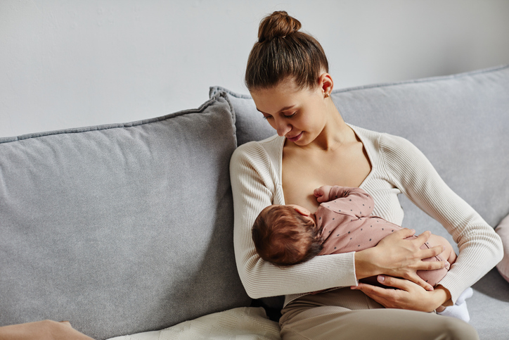 Une jeune mère allaite son bébé tout en se reposant sur un lit, représentant l'allaitement après des implants mammaires