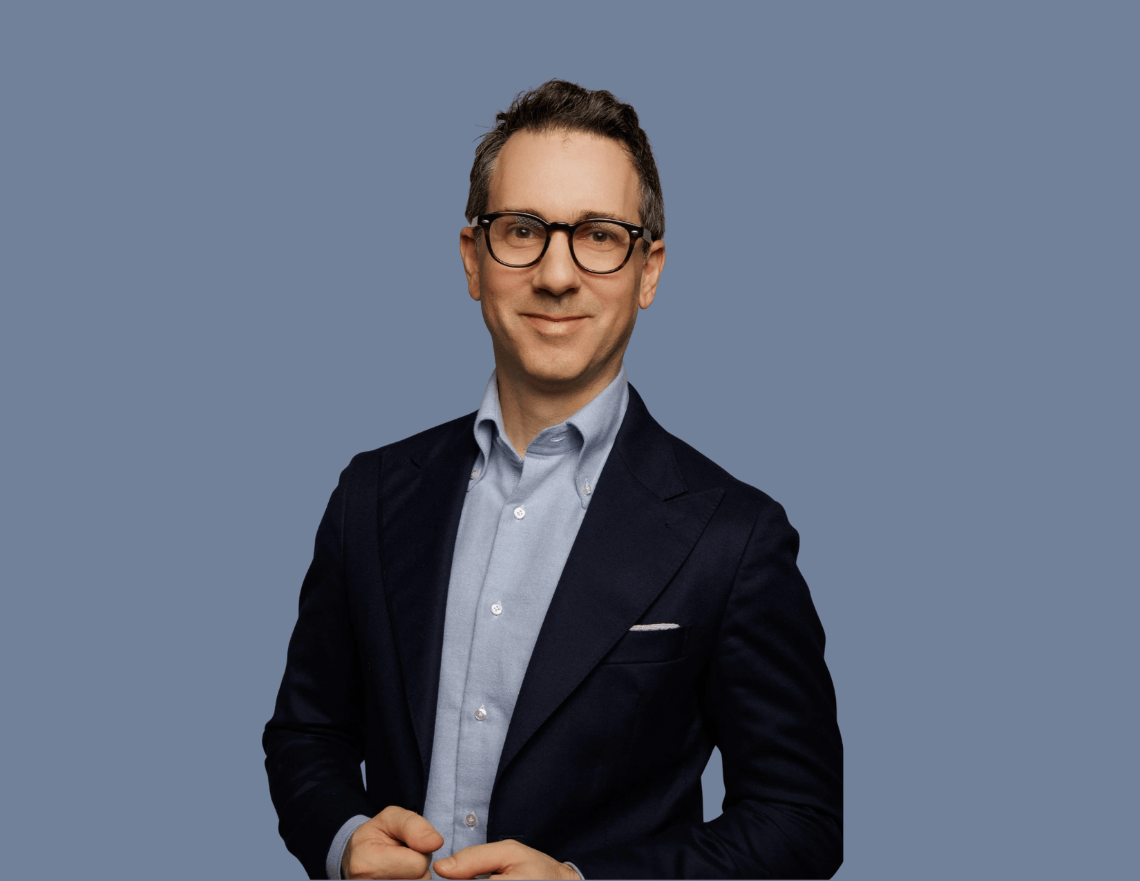 Professional portrait of a male physician in a navy blazer against a blue backdrop, used to illustrate an article on postpartum transformation featuring Dr. Guberman.