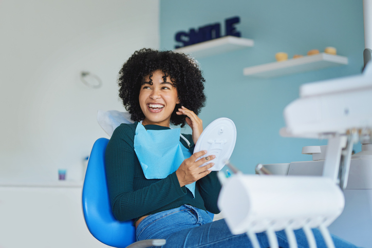 Femme souriante sur une chaise dentaire tenant un miroir lors d'une consultation d'implants dentaires All on 4 dans une clinique moderne.
