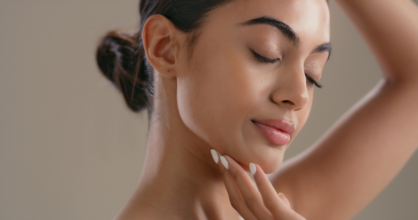 Gros plan d'une femme à la peau éclatante et uniforme, les yeux fermés, touchant doucement sa mâchoire, illustrant les résultats clairs et lumineux des soins Q Dermatology.