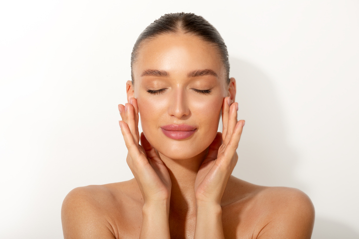 Une femme au teint éclatant se touche doucement le visage, illustrant les résultats du programme de soins de la peau réservé aux membres de Vanity Lab.